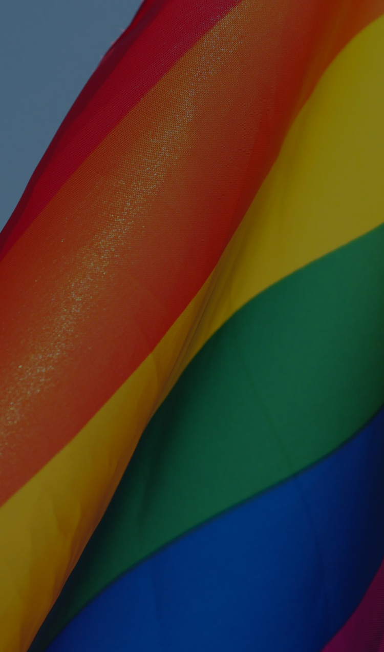 An inclusive pride flag partially folded in the wind.