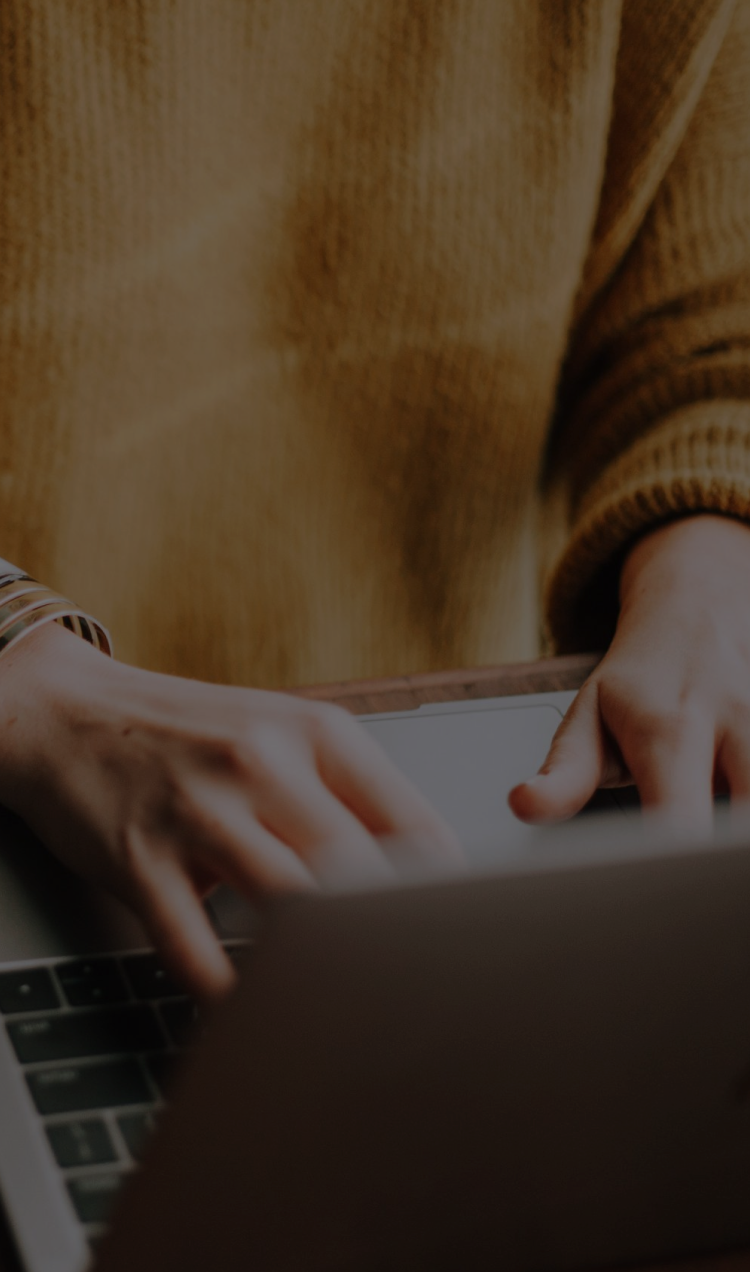 A woman in a mustard sweater researches on a silver laptop.