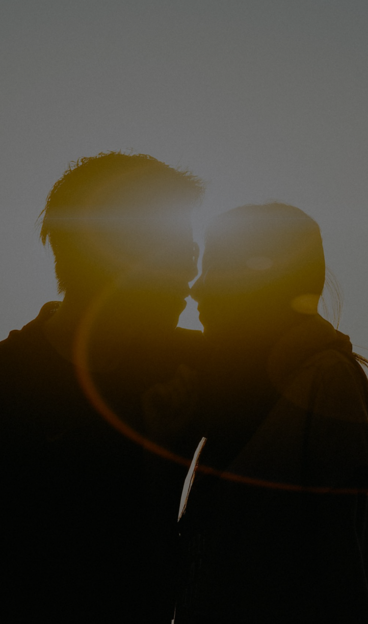 A couple embraces as silhouettes backlit by the sun.