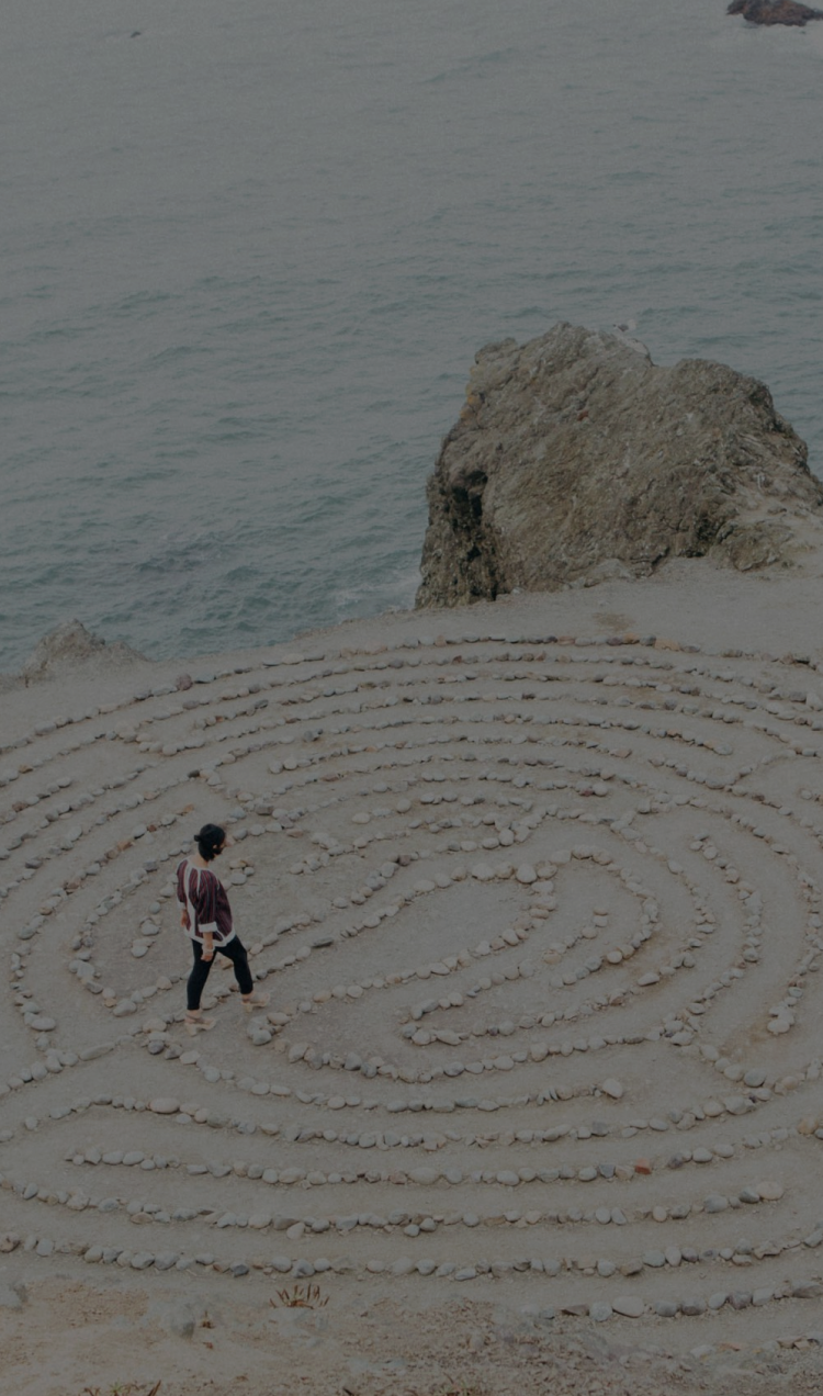 A man walks through a rock maze on a cliffside overlooking the ocean.