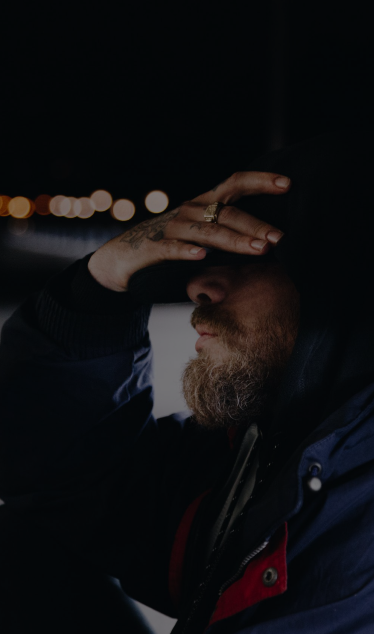 A man sits on the side of the road with his hand covering his face, looking visibly upset.